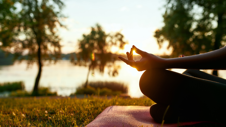 a women meditating on the grass in front of a lake 